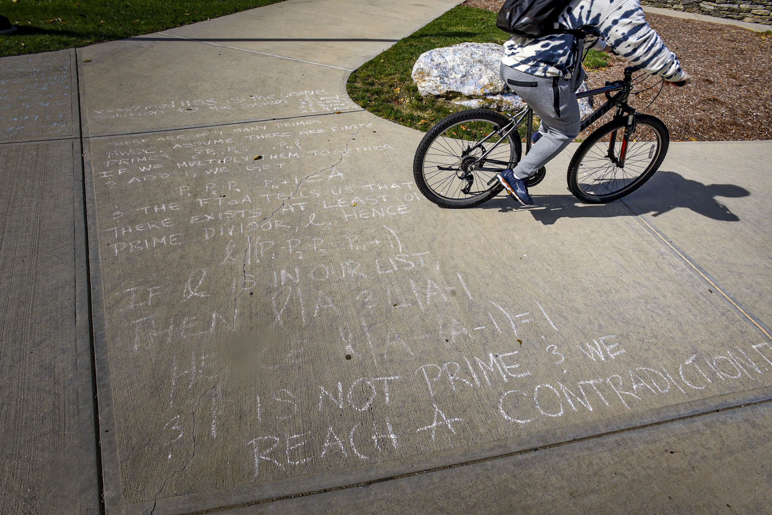 A mathematical proof, in chalk on a sidewalk, as a student rides by on a bicycle.